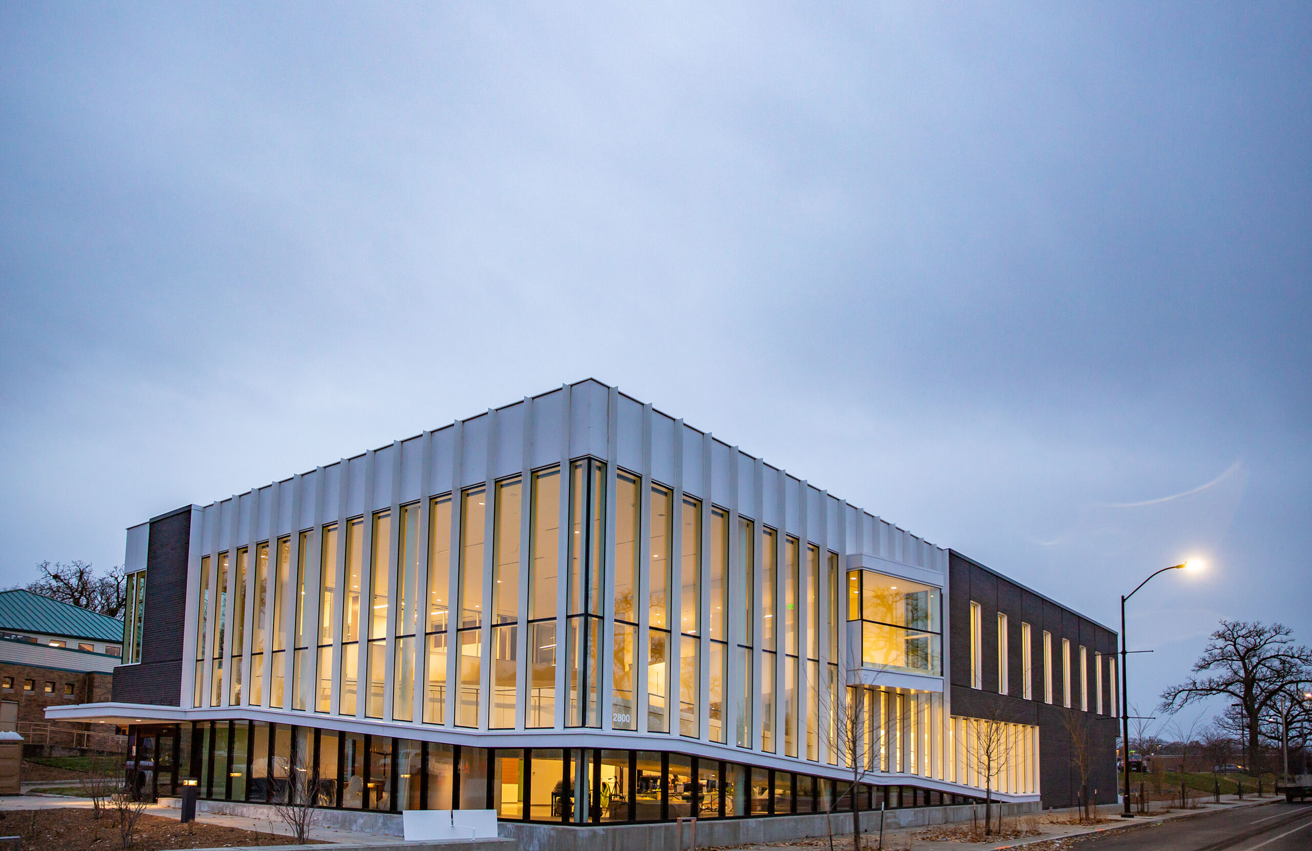 The new Harkin Institute building at dusk. Light shines through the two-story windows and the two-story ramp can be seen through the window.