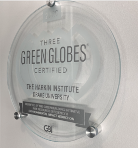 Circular plaque hanging in the entrance of the Tom and Ruth Harkin Center that reads: Three Green Globes Certified. The Harkin Institute. Drake University.