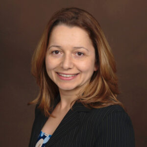 Headshot of Rayna Stoycheva. Rayna has shoulder-length brown hair and wears a suit jacket.